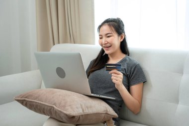 Kredi kartı sahibi serbest çalışan bir kadın, elinde kredi kartı ile banka uygulamasındaki bakiyeyi kontrol ederken aynı zamanda müşteriden sipariş almak için oturuyordu.