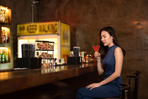 Beautiful woman is drinking cocktail and having enjoy to relaxing while sitting alone to listening music on counter bar in restaurant or hotel bar