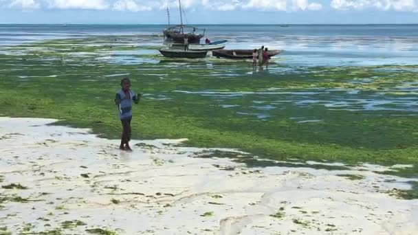 NUNGWI, ZANZIBAR, 2018年2月19日-漁船の前を歩く男の子 — ストック動画
