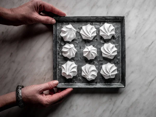 Female hands holdging baking pan with white meringue from egg and snowlakes. Overhead shot.