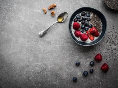 Yoğurt ve meyveli mavi kase. Ballı kaşık, ceviz ve chia çekirdeği. Fotokopi alanı ile genel çekim.