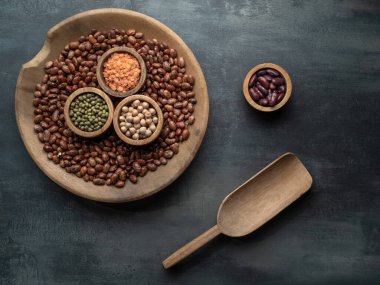 Bir kase kurutulmuş baklagil, fasulye, mercimek ve gri masadaki ahşap kepçeli nohut. Yemek arkaplanı. Fotokopi alanı ile genel çekim.