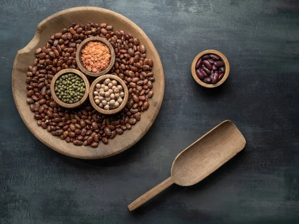 Bir kase kurutulmuş baklagil, fasulye, mercimek ve gri masadaki ahşap kepçeli nohut. Yemek arkaplanı. Fotokopi alanı ile genel çekim.