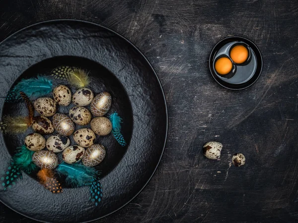 Easter concept. Quail eggs, golden eggs and bowl of colorful feathers. Bowl of two yolks and crushed eggshell on vintage background. Overhead view.