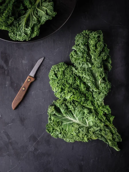 Fresh green kale leaves in black bowl and knife on dark table. Overhead shot witch copy space.