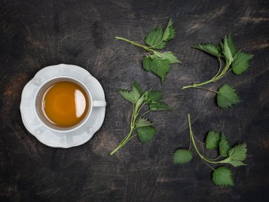 Taze ısırgan otu - urtica dioica - beyaz seramik bardakta çay, ahşap şarap masasında. Fotokopi alanı ile genel çekim.