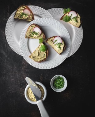 Avokado soslu ekmek, üç beyaz tabakta turp ve taze soğan. Fotokopi alanı ile üstten çekim. Karanlık ve karamsar.