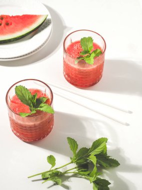 İki bardak kırmızı karpuz püresi ve beyaz masada taze nane yaprakları. Boşluğu kopyala.