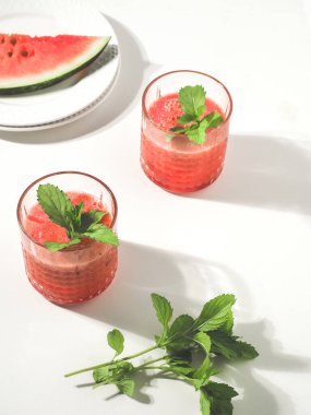 İki bardak karpuz kırmızısı smoothie ve taze nane yaprağı beyaz masa.
