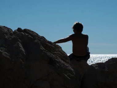 Güneş gözlüklü beyaz çocuk gün batımında bankada oturuyor. Arkaplan.