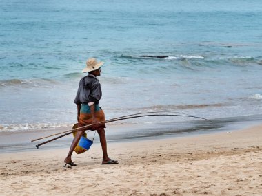 MIRISSA, SRI LANKA - 17 Mart 2019: Sıska Asyalı balıkçı hasır şapka ve oltayla sahilde yürüyor.