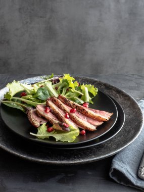 Kızarmış ördek göğsü, yeşil salata ve siyah tabakta nar.-