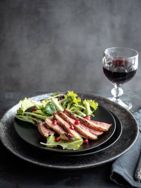 Kızarmış ördek göğsü, yeşil salata ve siyah tabakta nar..