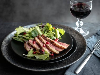 Kızarmış ördek göğsü, yeşil salata ve siyah tabakta nar..