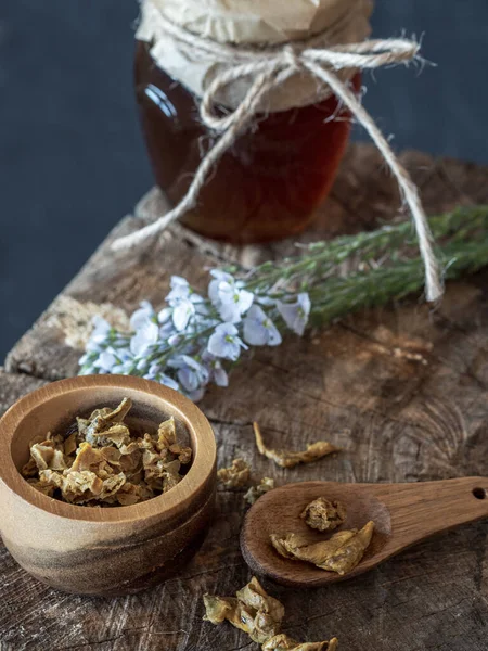 Tarro de miel, flores y cuenco de madera de gránulos de propóleos en pieza de madera. — Foto de Stock