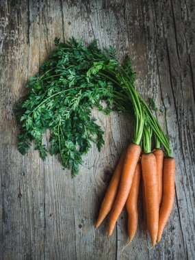 Tahta zemin üzerinde yeşil yapraklar olan taze havuç sürüsü. Fotokopi alanı ile genel çekim.