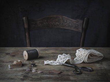Dikiş aletleri olan eski ahşap masa - eski makas, dantel, ahşap iplik makarası, mezura. Karanlık ve karamsar. 
