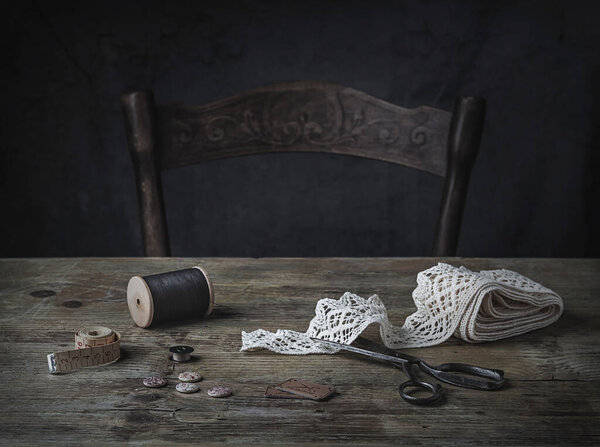Старый деревянный стол с швейными инструментами - винтажные ножницы, кружева, деревянная катушка из ниток, рулетка. темные и капризные. 