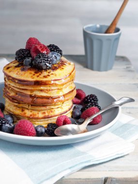 Taze böğürtlenli krep - yabanmersini, ahududu ve böğürtlen - ve bal tabakta ve beyaz ahşap masa.