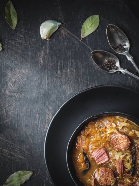 Siyah tabakta sosisli lahana çorbası, koyu arkaplanda sarımsak ve karabiber. Genel çekim ve kopyalama alanı.