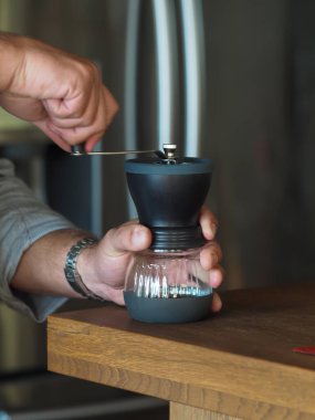 Erkek eller kahve öğütücüsünü ahşap masada yuvarlıyor. Kapatın. Sığ alan derinliği. 