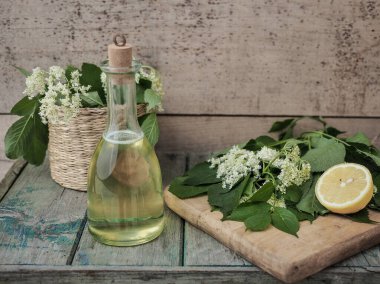 Ahşap masada şişede ev yapımı yaşlı çiçek şurubu. Kesme tahtasında taze yaşlı çiçek ve limon. Boşluğu kopyala.