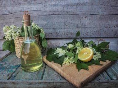 Ahşap masada şişede ev yapımı yaşlı çiçek şurubu. Kesme tahtasında taze yaşlı çiçek ve limon. Boşluğu kopyala.