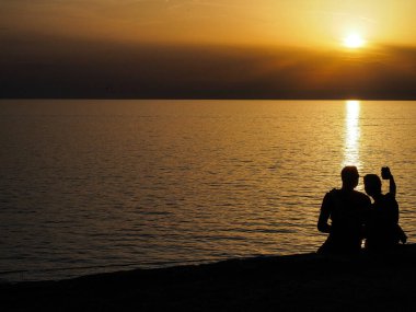 Sahilde oturup gün batımında selfie çeken romantik çiftlerin silueti.. 