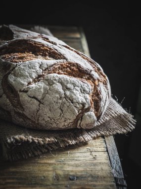 Ahşap masada taze pişmiş ekmek. Karanlık ve karamsar. Boşluğu kopyala.