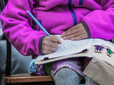 Mavi kapüşonlu bir kız sandalyede oturuyor ve mavi kalemle kağıda çiziyor..