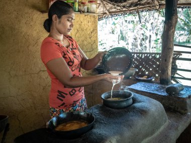 HIRIWADUNNA, SRI LANKA - 10 Mart 2019: Geleneksel kırsal mutfakta pirinç ve köri pişiren genç Güney Asyalı kadın. Eko Köyü Hiriwadunna.