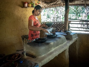 HIRIWADUNNA, SRI LANKA - 10 Mart 2019: Geleneksel kırsal mutfakta pirinç ve köri pişiren genç Güney Asyalı kadın. Eko Köyü Hiriwadunna.