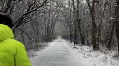 Sarı ceketli adam kış karları boyunca ormanda yürür. Arkadan ileri doğru atış. Yüksek kalite 4k görüntü.