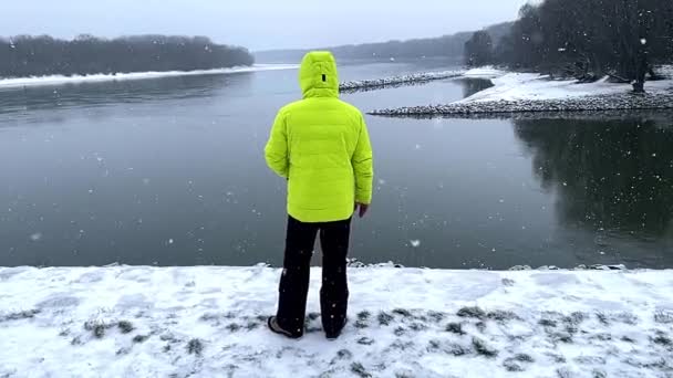 黄色のジャケットの男はドナウ川を見ている 冬の降雪 前進は後ろから撃たれた 高品質のフルHd映像 スローモーション — ストック動画