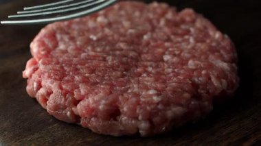 Çatal, hamburgere hazır ahşap kesme tahtasındaki çiğ sığır pirzolasının dokusunu yapıyor. Ağır çekim. Tam HD görüntüler