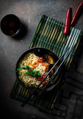 Geleneksel Japon çorbası, karidesli ramen, Asya eriştesi, koyu arkaplanda midye biberi. Asya usulü yemek. Mesaj için yer var. Deniz mahsullü erişte ve mikroyeşil