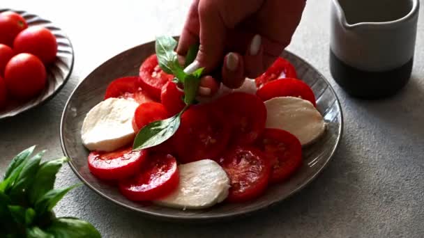 Put basil on caprese salad. Tomato salad with mozzarella and basil leaves. Italian cuisine. Mediterranean lunch. Organic food. Italian caprese. — Stock Video