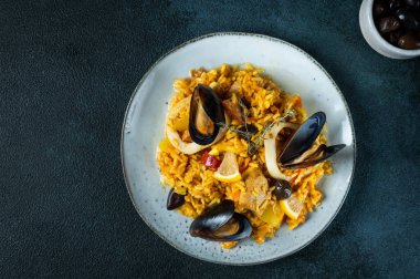 İspanya 'nın klasik yemeği, deniz ürünleri paella tabağı ve mavi arka plan manzarası. İspanyol paellası, karides, kıskaç, midye ve taze limon. İspanyol yemeği. Rahatlatıcı yemek. Deniz mahsullü pilav