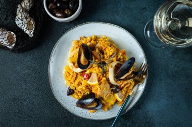 İspanya 'nın klasik yemeği, deniz ürünleri paella tabağı ve mavi arka plan manzarası. İspanyol paellası, karides, kıskaç, midye ve taze limon. İspanyol yemeği. Rahatlatıcı yemek. Deniz mahsullü pilav
