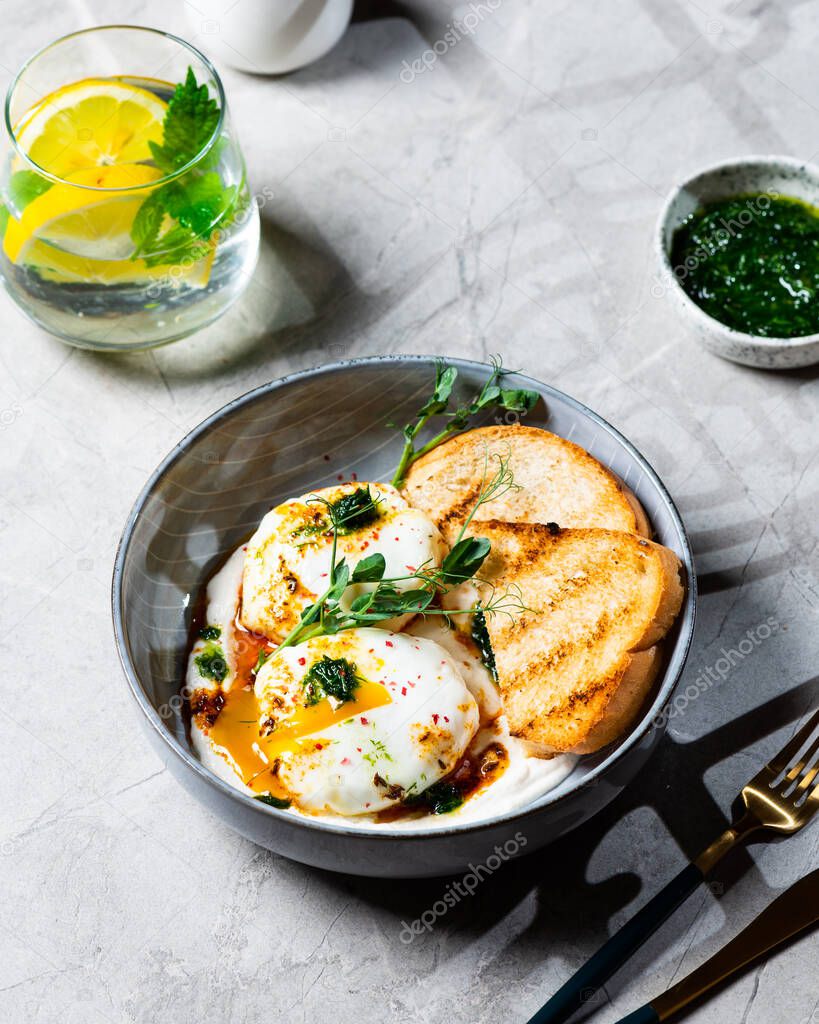 Cilbir or Turkish Eggs. dish served as mezze: poached eggs topped over herbed greek yogurt, then drizzled with hot spiced paprika olive oil. Turkish breakfast in a grey bowl on marble background.