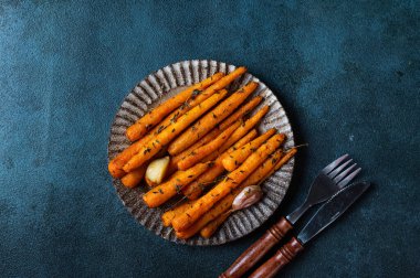 Kızarmış havuç yemeye hazır. Otlu havuç ve sarımsaklı üst manzara. Koyu arkaplanda kızarmış havuç. Sotelenmiş sebzeler. Rahatlatıcı yemek. Sürdürülebilir tüketim.