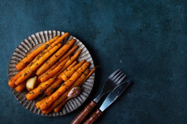 Kızarmış havuç yemeye hazır. Otlu havuç ve sarımsaklı üst manzara. Koyu arkaplanda kızarmış havuç. Sotelenmiş sebzeler. Rahatlatıcı yemek. Sürdürülebilir tüketim.