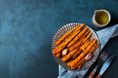 Kızarmış havuç yemeye hazır. Otlu havuç ve sarımsaklı üst manzara. Koyu arkaplanda kızarmış havuç. Sotelenmiş sebzeler. Rahatlatıcı yemek. Sürdürülebilir tüketim.