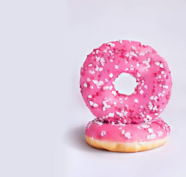 Beyaz arka planda şeker kırıntılarıyla kaplı iki pembe donut yakın plan izole edilmiş. Yatay kare görünümü.