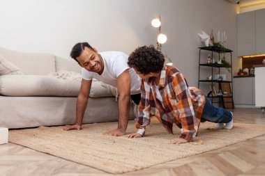 Afrikalı Amerikalı bir adam ve oğlu şınav çekiyorlar ve evde antrenman yapıyorlar. Gençler ve babası birlikte spor yapıyor ve spor yapıyorlar.