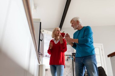Yaşlı çift mutfakta buzdolabı kullanıyor, gri saçlı kadın ve kocası mutfakta yemek pişiriyor ve buzdolabından sebze alıyorlar.