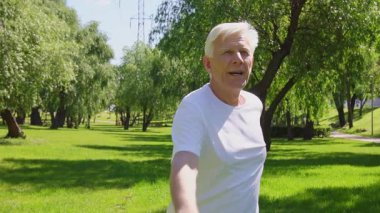 Yaşlı yaşlılar parkta pilates yapıyor, yaşlı gri saçlı emekliler dışarıda yoga yaparken kollarını kaldırıyor.