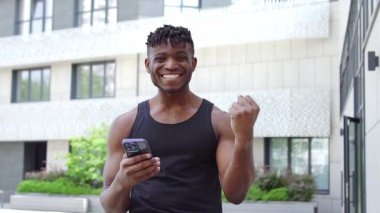 Afro-Amerikalı atlet akıllı telefon kullanıyor ve zaferini internette kutluyor, sporcu adam cep telefonunu tutuyor ve başarısından keyif alıyor.