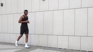 Genç Afro-Amerikalı adam dışarıda koşuyor ve kulaklıklı atletik adam şehir duvarına karşı spor yapıyor.