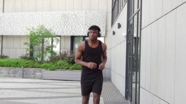 Genç Afro-Amerikalı adam dışarıda koşuyor ve kulaklıklı atletik adam şehir duvarına karşı spor yapıyor.